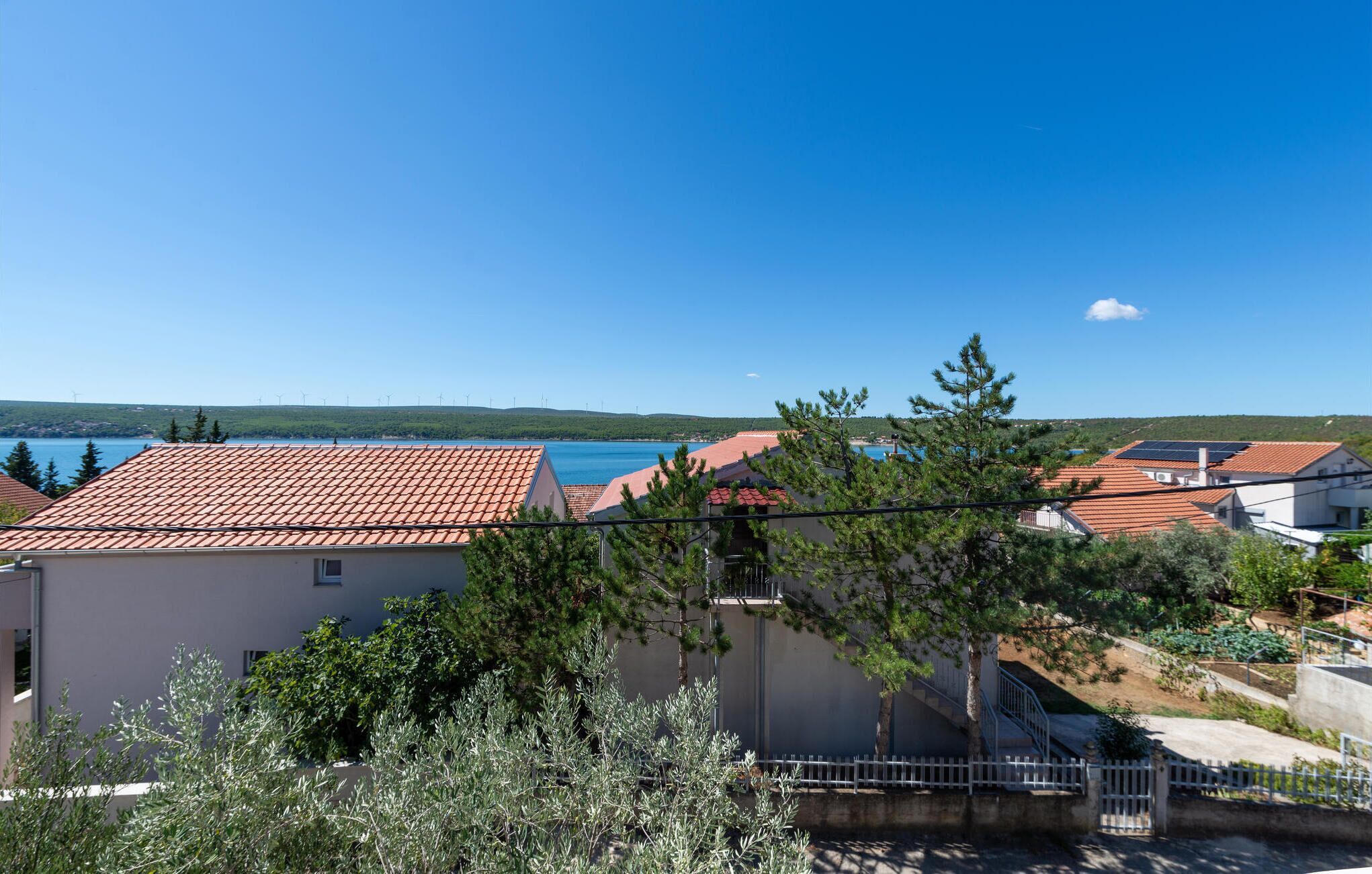 Un área residencial costera con tejados de tejas de color terracota, un cielo azul despejado y vista al mar.