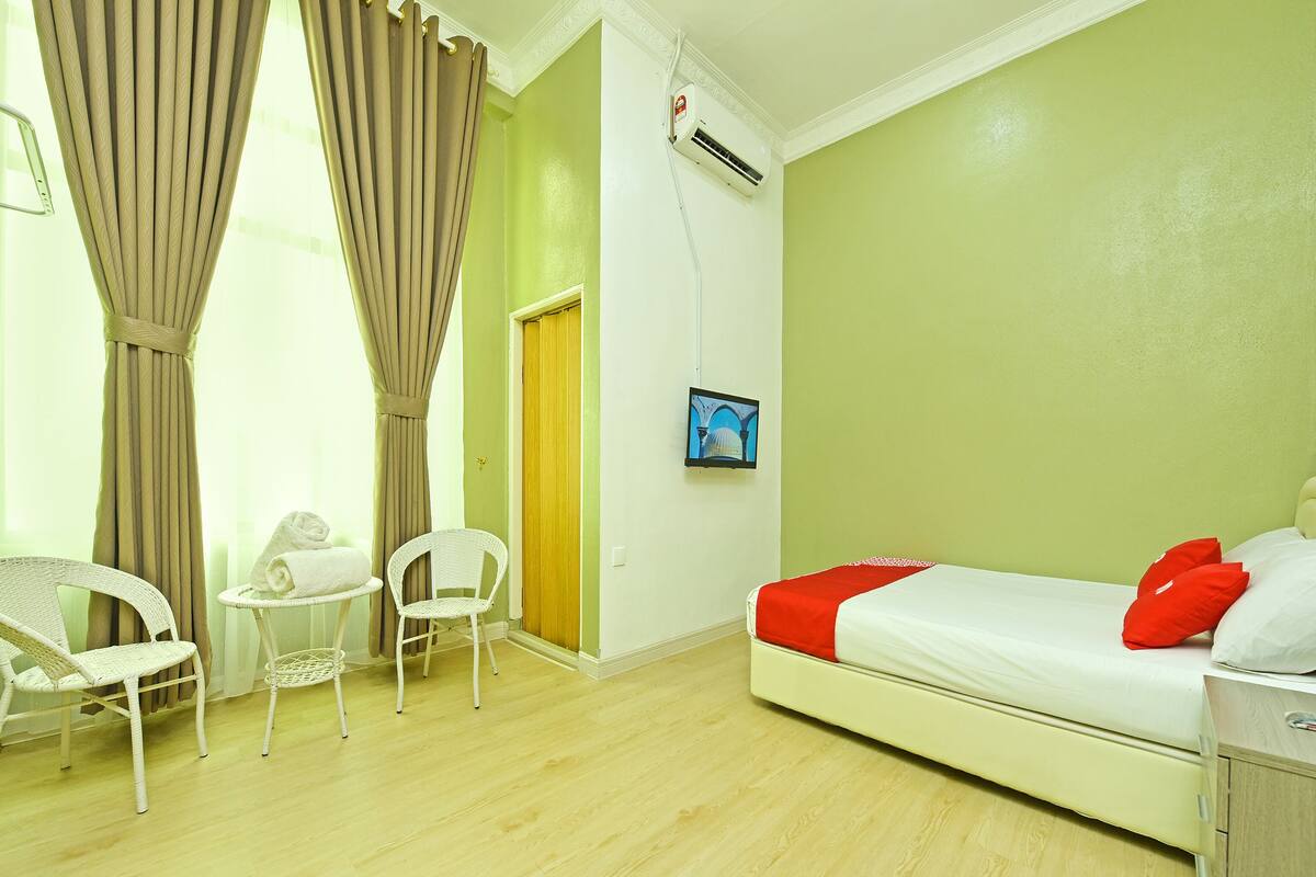 A hotel room with a bed, two chairs, a small table, a door, and a wall-mounted air conditioner.