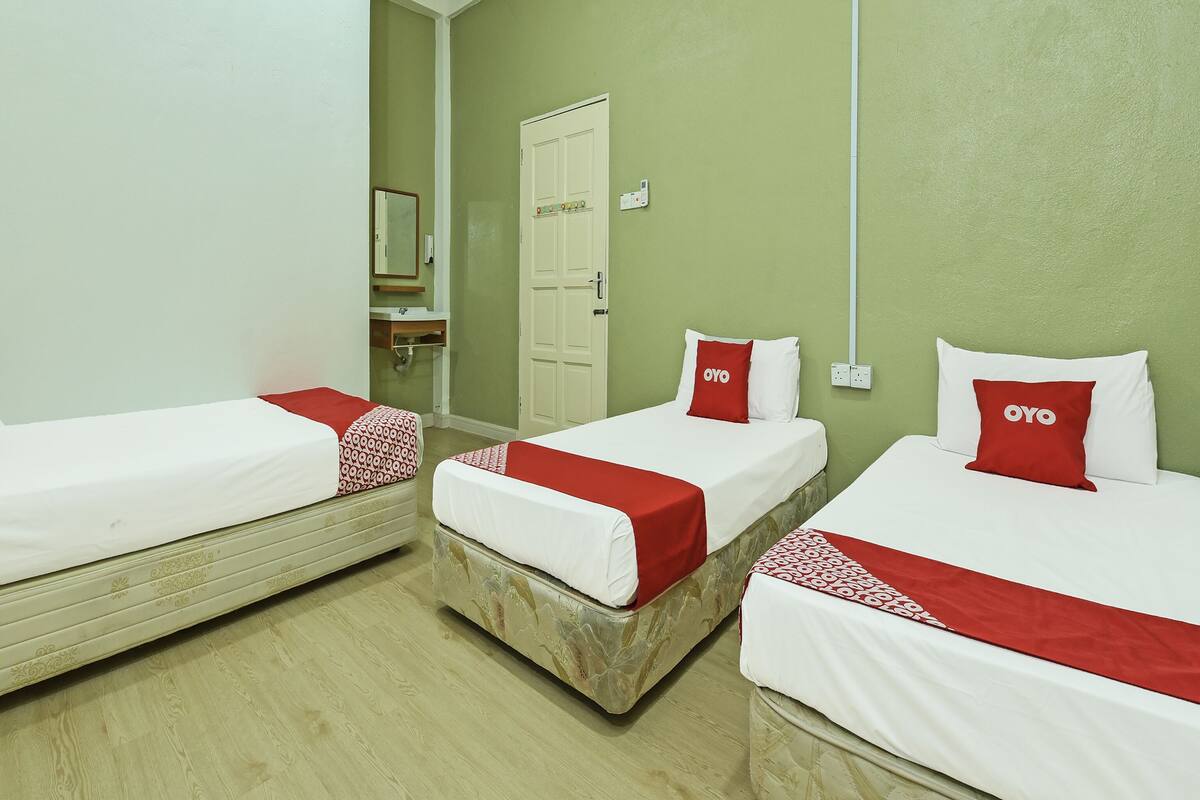 A hotel room with three single beds, each with a red and white bedspread and a pillow with the word "OYO".