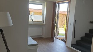 A spacious room with a large window, a radiator, a staircase, and a door leading outside. - Schöne Ruhige Ferienwohnung mit Terrasse (Flensburg)