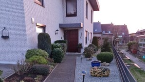 A modern house with a brick exterior, a paved driveway, and a well-maintained garden with various plants and a small pathway. - Schöne Ruhige Ferienwohnung mit Terrasse (Flensburg)