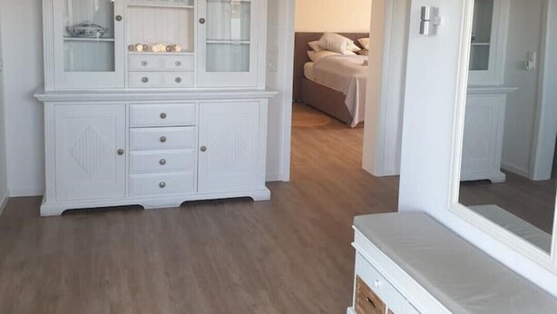 A room with a white cabinet with glass doors, a bed with a headboard, and a mirror on the wall. - Schöne Ruhige Ferienwohnung mit Terrasse (Flensburg)