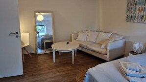 A modern hotel room with a white sofa, a small round table, and a bed with a neatly made bedspread. - Schöne Ruhige Ferienwohnung mit Terrasse (Flensburg)