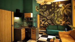 A compact kitchen with a checkered floor, a green sofa, and a tropical leaf mural. - Jungle Apartments (Wroclaw)