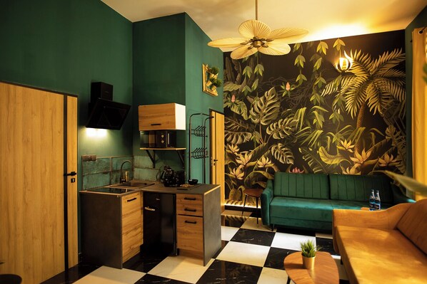 A compact kitchen with a checkered floor, a green sofa, and a tropical leaf mural. - Jungle Apartments (Wroclaw)