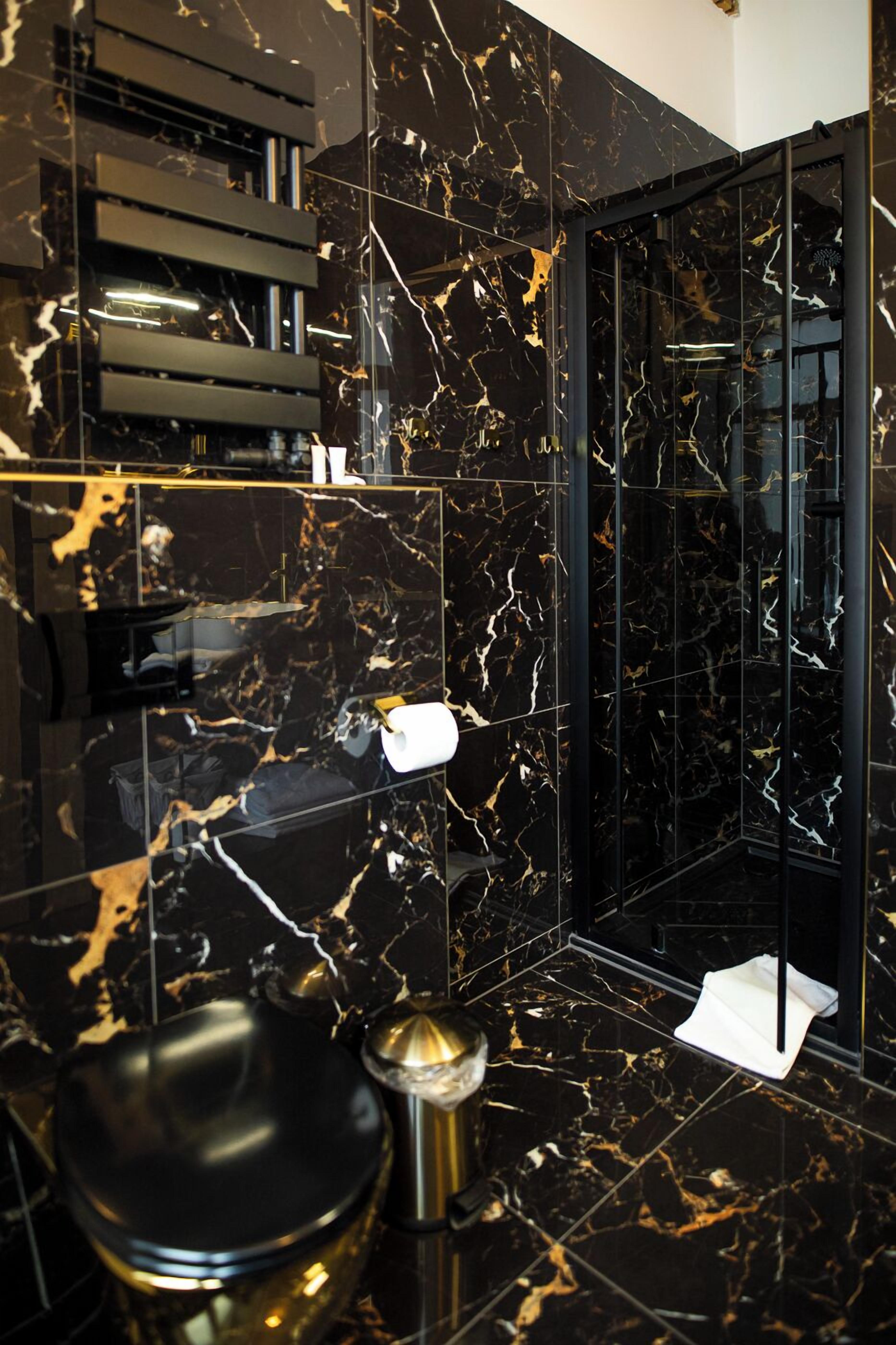 Ein modernes Badezimmer mit schwarzen Marmorfliesen, einer schwarzen Toilette und einer gläsernen Duschkabine.