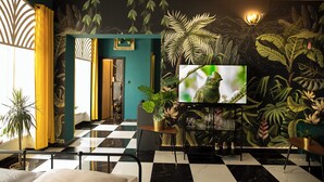 A room with a checkered floor, a television, and a wall with a tropical mural. - Jungle Apartments (Wroclaw)
