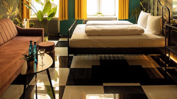 A hotel room with a checkered floor, a bed, a sofa, a ceiling fan, and a window with curtains. - Jungle Apartments (Wroclaw)