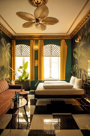 A hotel room with a checkered floor, a bed, a sofa, a ceiling fan, and a window with curtains. - Jungle Apartments (Wroclaw)