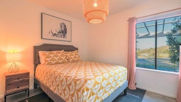 A bedroom with a bed, a nightstand, a lamp, a window with a view, and a hanging light fixture.