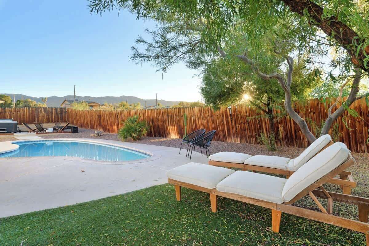 A backyard with a swimming pool, lounge chairs, and a wooden fence.