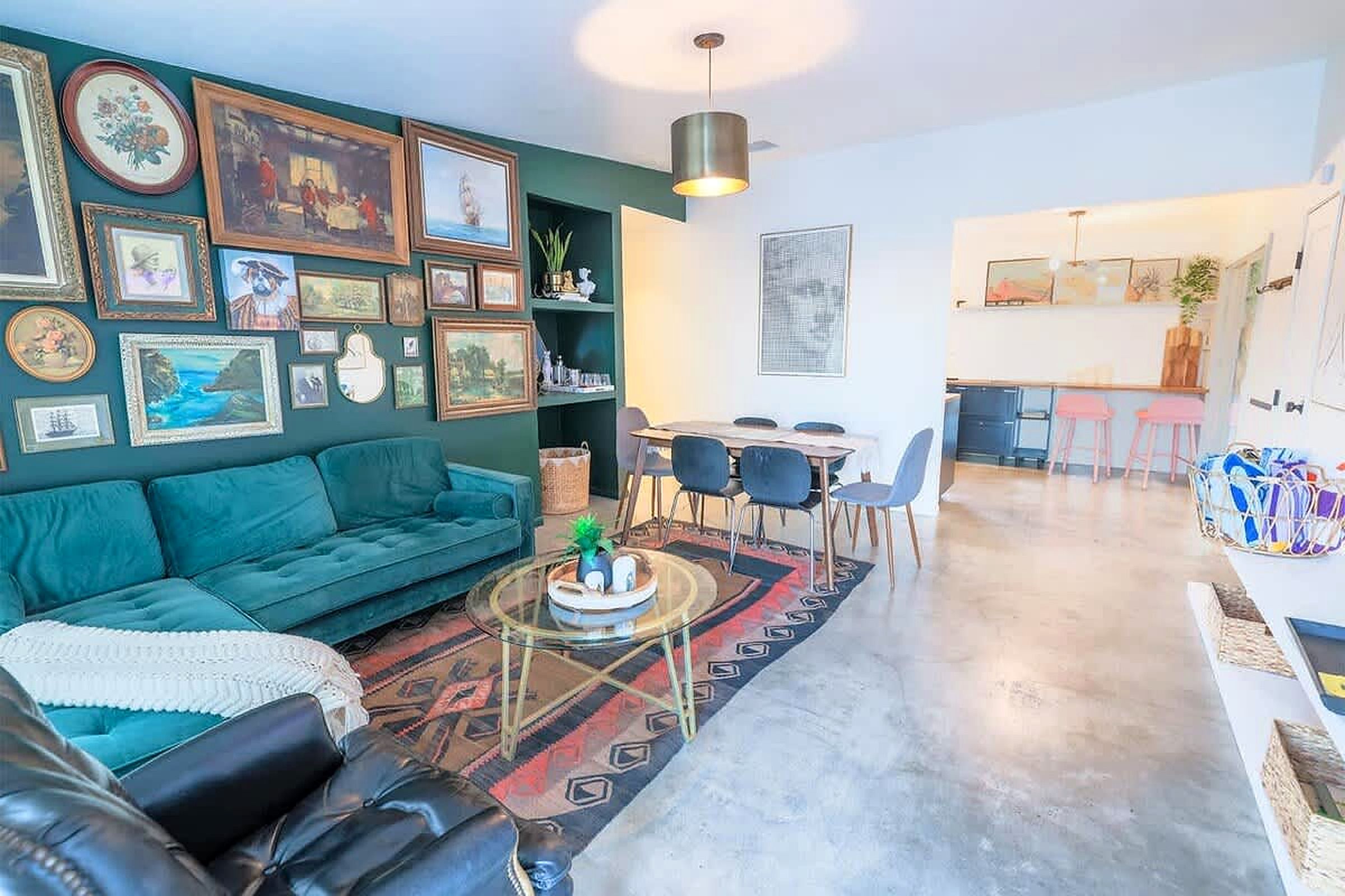 A modern living room with a teal sofa, a glass coffee table, and a dining area with chairs and a table.