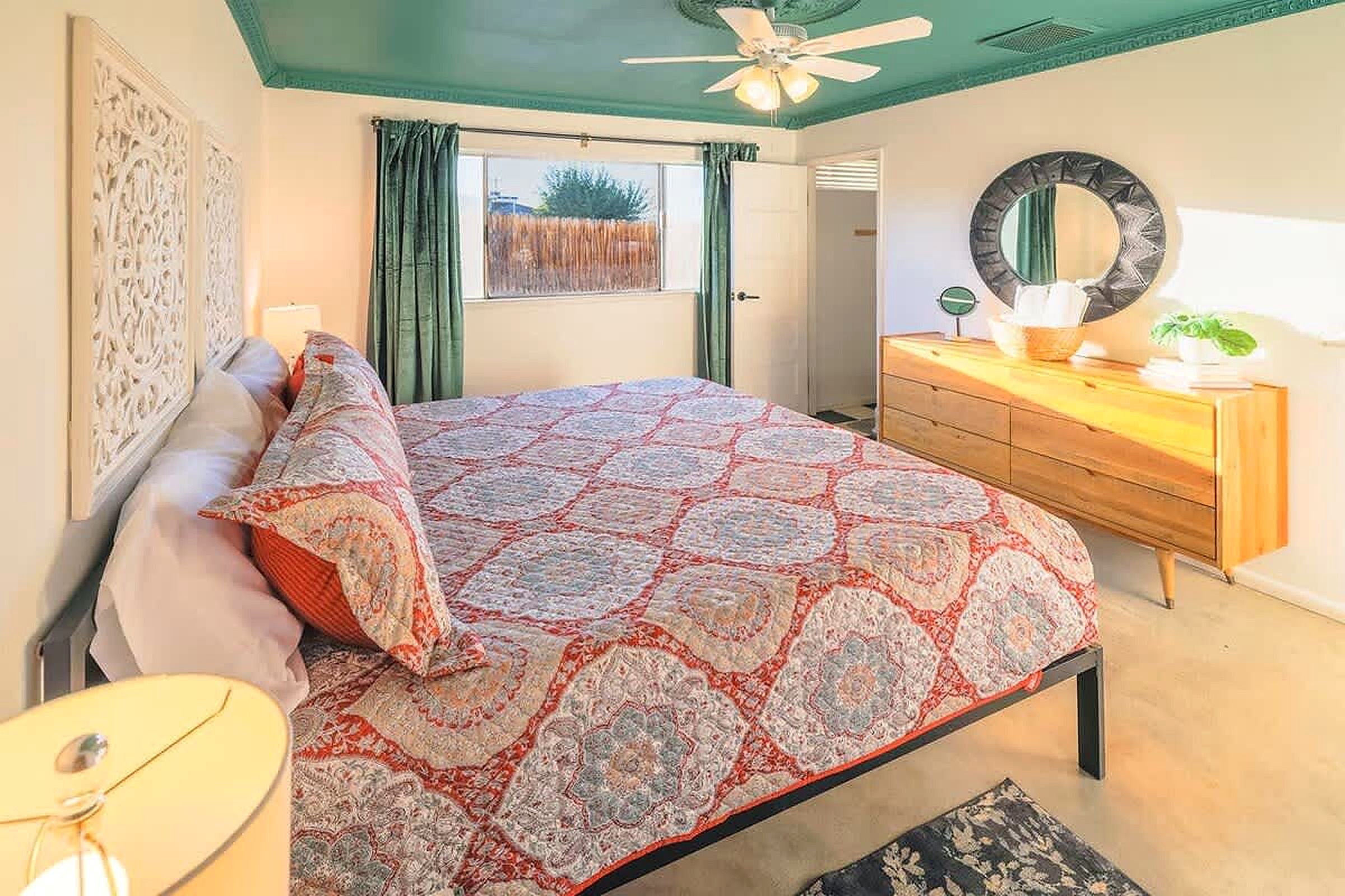 A bedroom with a bed, a dresser, a mirror, and a ceiling fan.