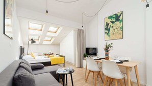 A modern, well-lit room with a sofa, dining table, and a bed with skylights.
