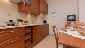 Una cocina compacta con armarios de madera, microondas y una mesa de comedor con mantel de encaje.