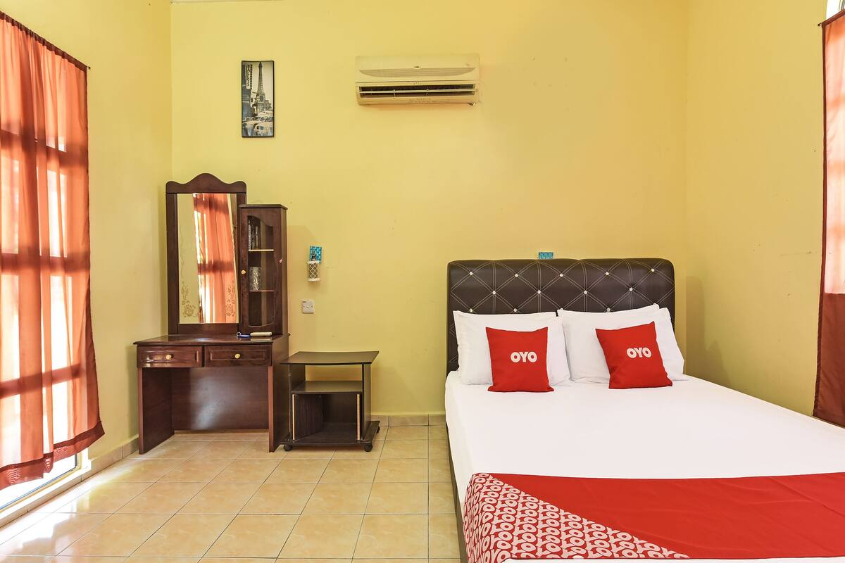 A hotel room with a bed, a desk, a wardrobe, and an air conditioning unit.