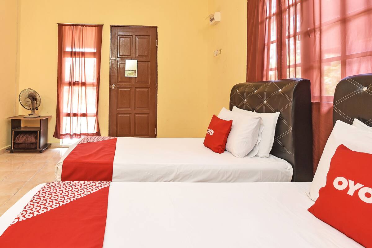 A hotel room with two beds, a wooden door, and a fan.