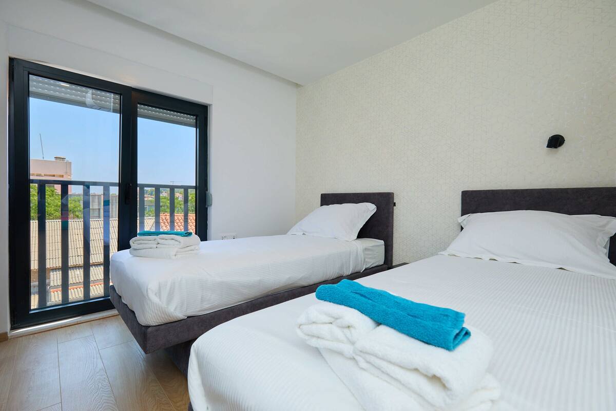 A hotel room with two beds, a balcony, and a view of the cityscape.