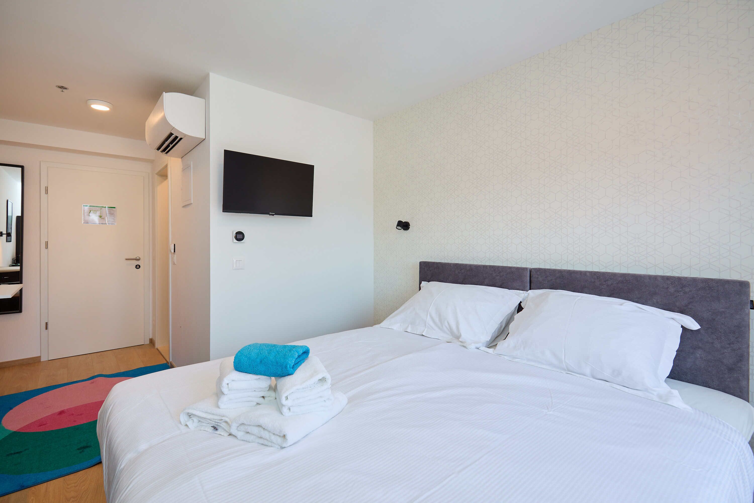 Quarto de hotel com cama, televisão de tela plana na parede e porta com espelho.