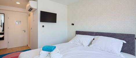A hotel room with a bed, a flat-screen TV mounted on the wall, and a door with a mirror.