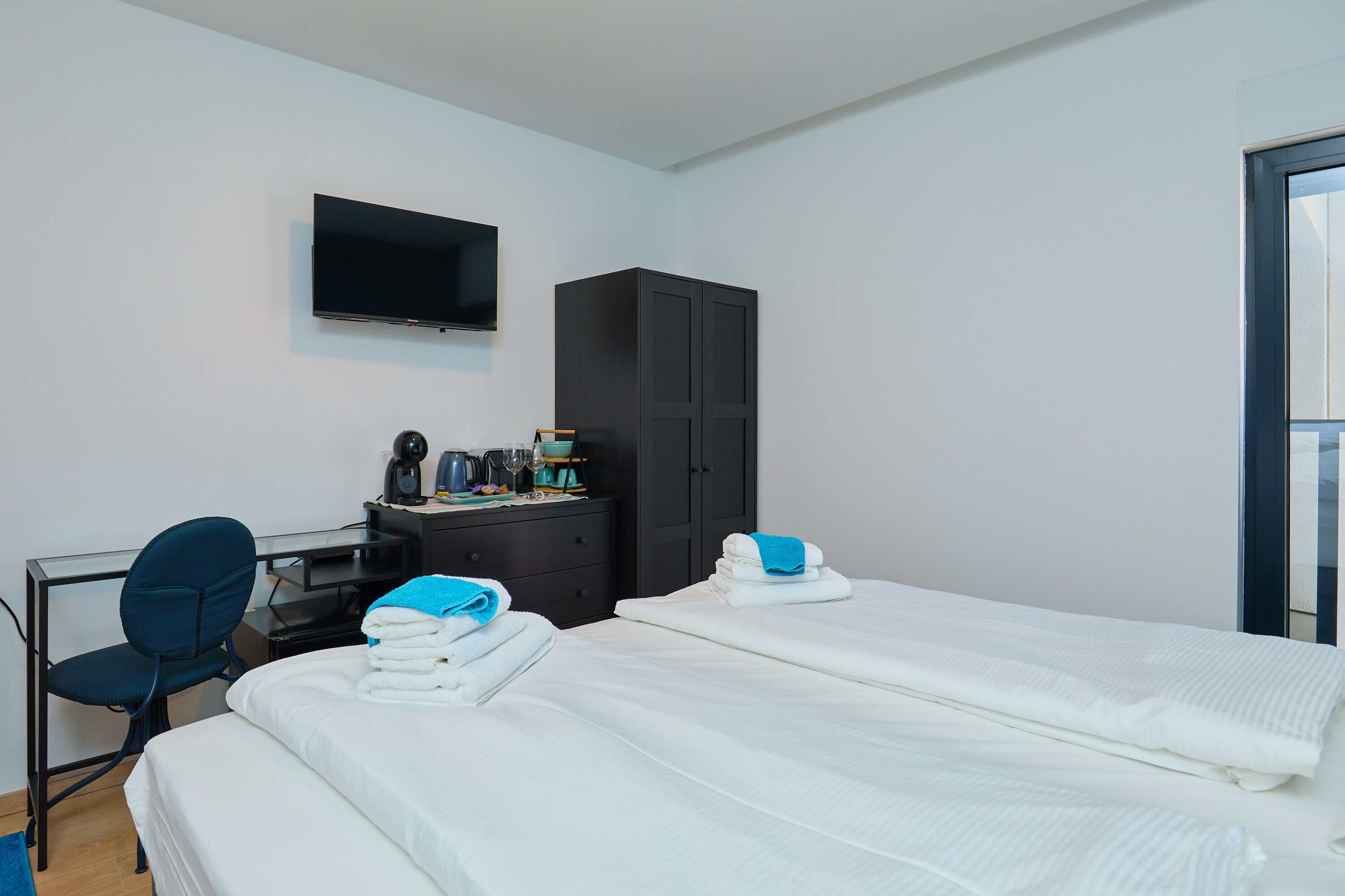 Quarto de hotel com duas camas, uma escrivaninha, uma cadeira, um guarda-roupa e uma TV de tela plana.