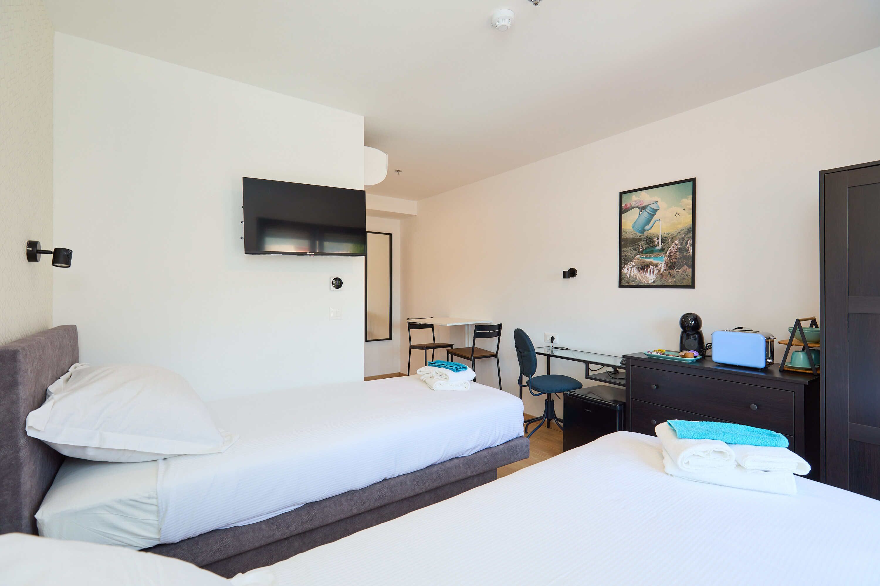 A hotel room with two beds, a desk, a chair, a TV, and a painting on the wall.
