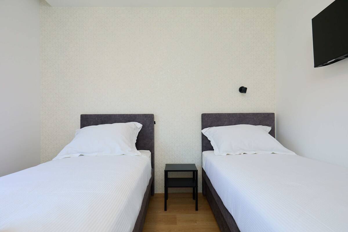 A hotel room with two single beds, a small bedside table, and a wall-mounted TV.