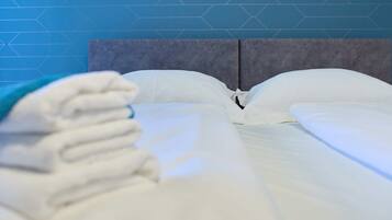 A neatly made bed with white linens and a grey headboard against a blue wall with a geometric pattern.