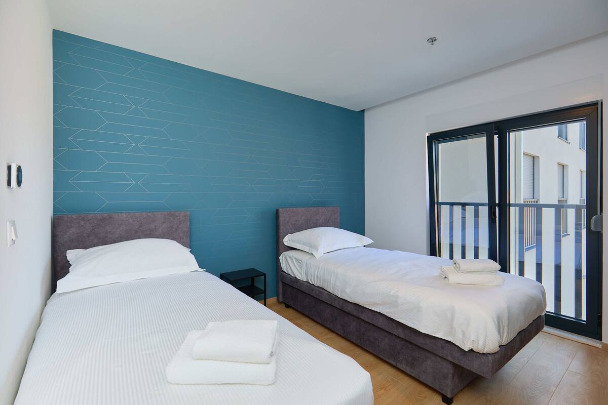 A hotel room with two beds, a blue accent wall, and a sliding glass door to the outside.