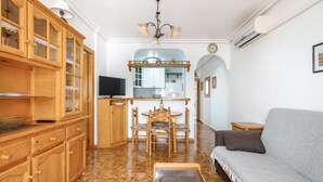 Una sala de estar con armarios de madera, un televisor, una mesa de comedor con sillas, un sofá y una mesita con una lámpara.