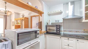 Cocina funcional con microondas, tostadora y horno. Cuenta con gabinetes blancos y un estante de madera sobre la encimera.