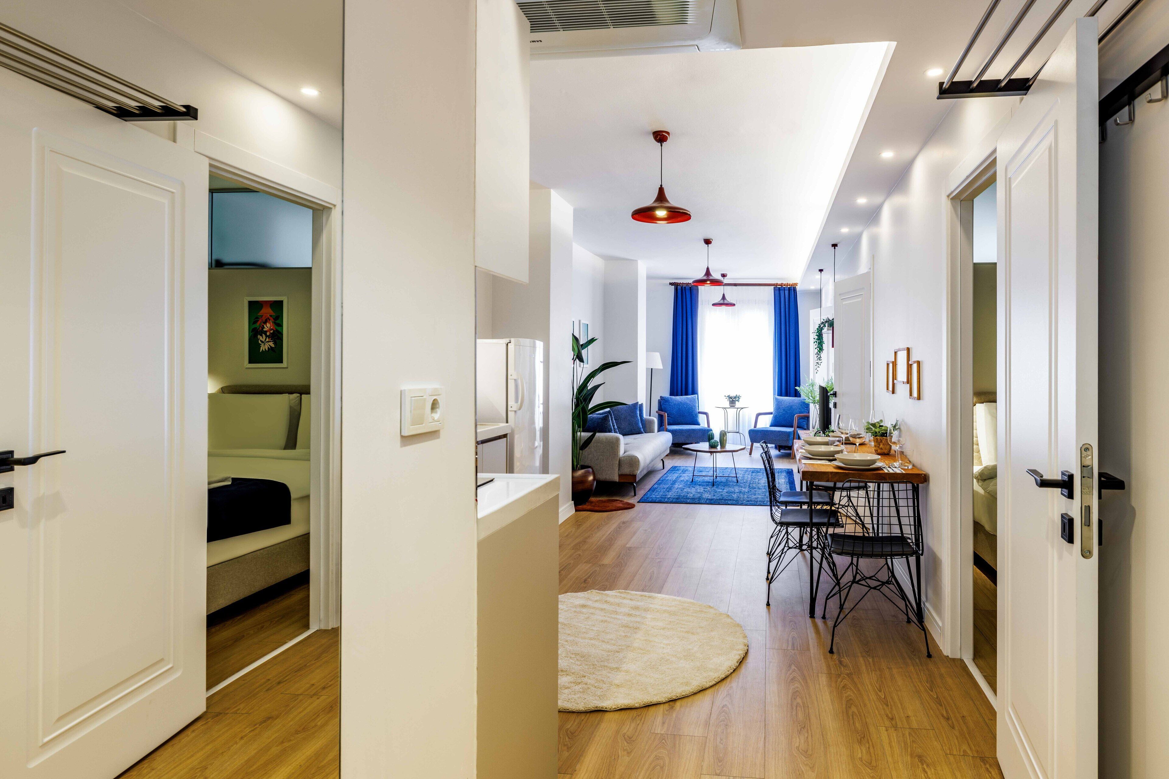 Un salon moderne avec un coin repas, un parquet et une grande fenêtre ornée de rideaux bleus.