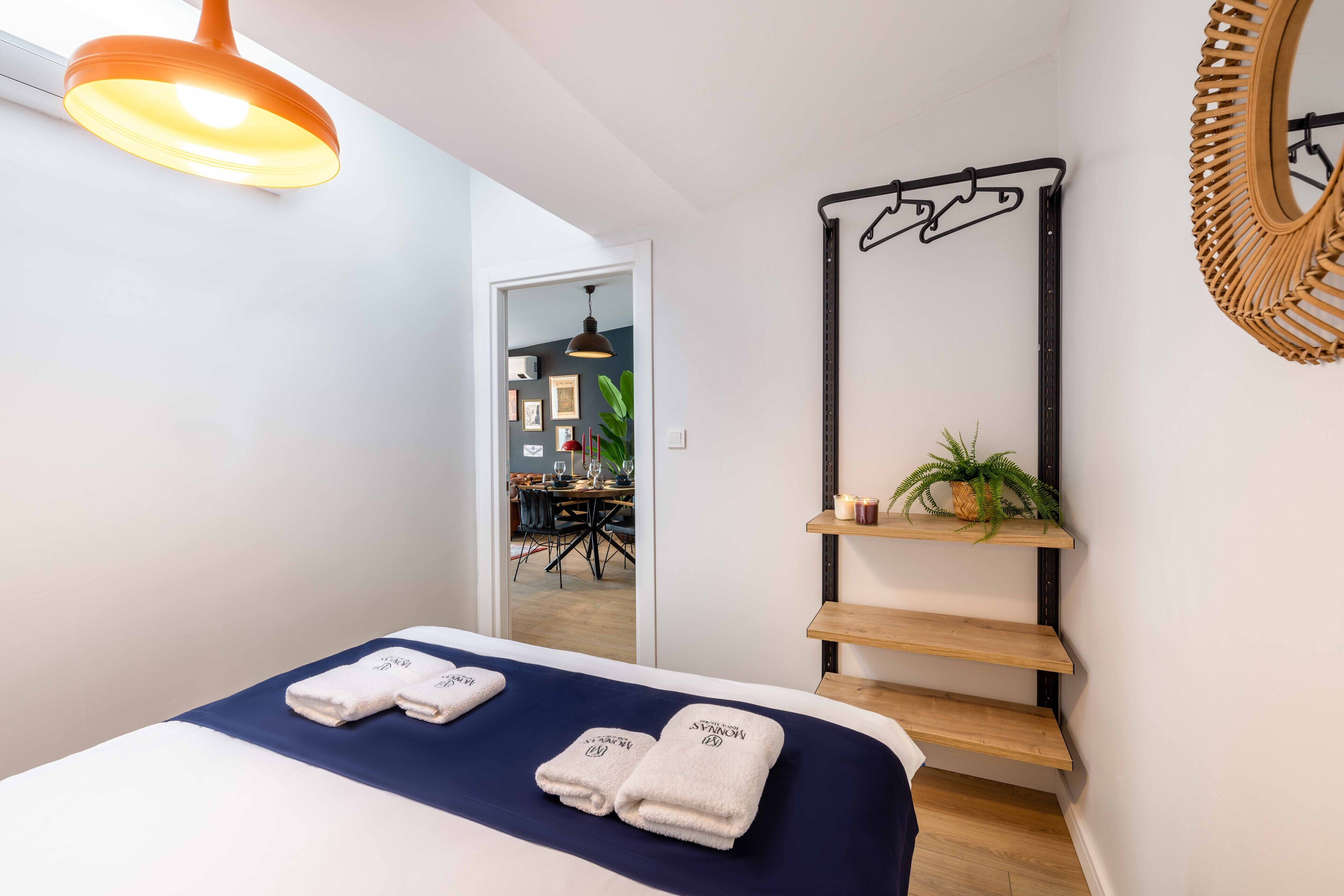 Une chambre d’hôtel avec un lit, un luminaire suspendu, un miroir et un escalier orné d’une plante.