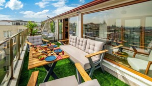 Terraço no topo com mesa posta para refeição, assentos acolchoados e vista para a paisagem urbana.