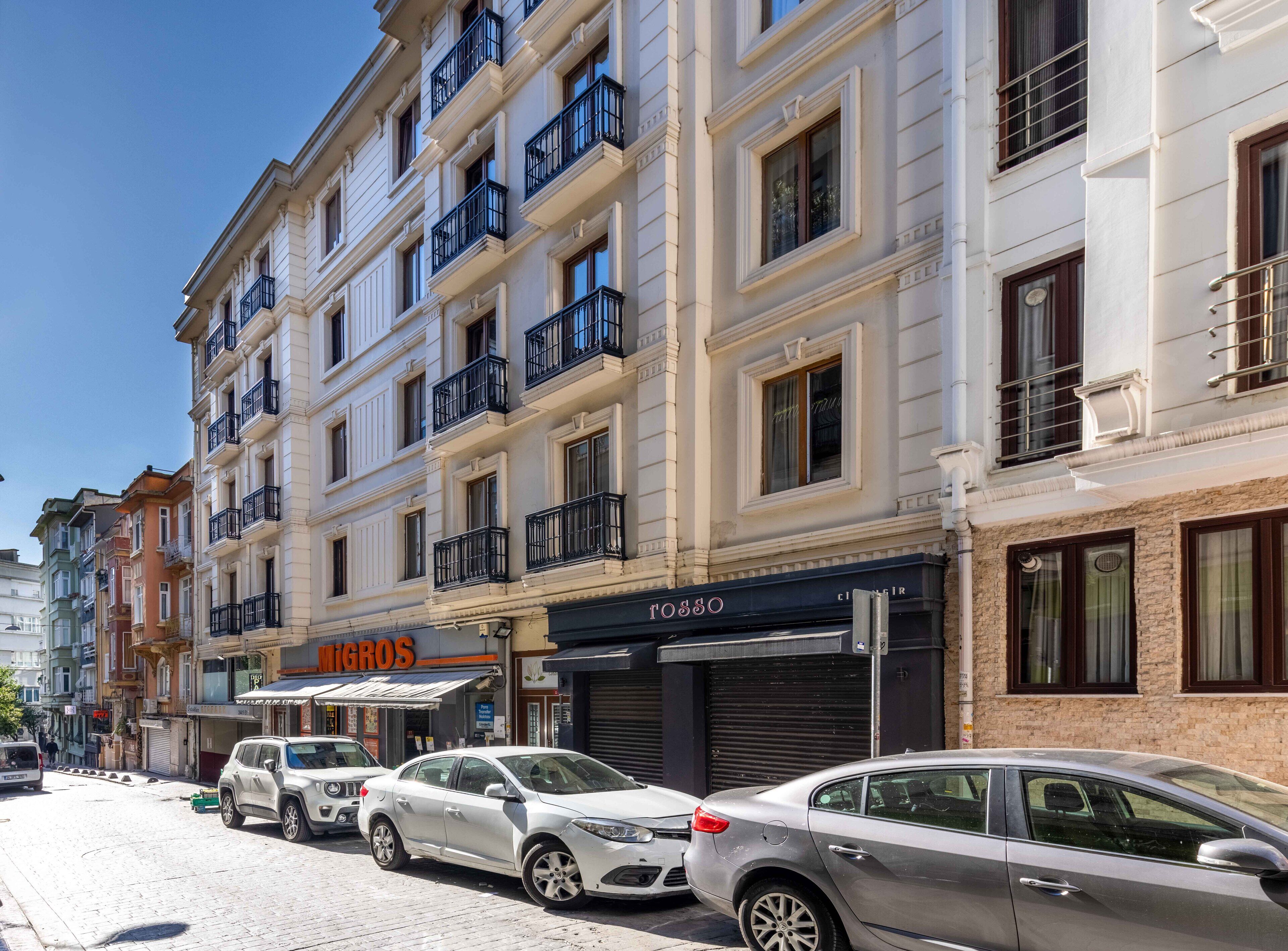 A multi-story building with balconies, storefronts, and parked cars on the street.