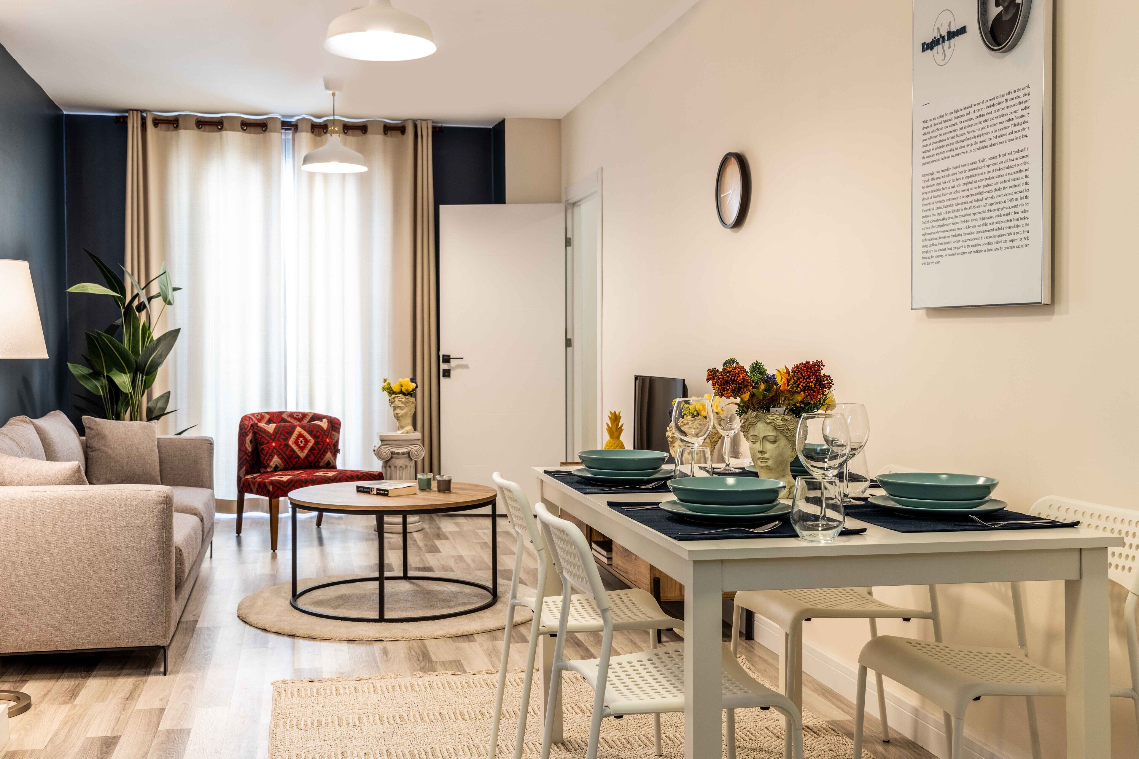 Un salon moderne comprenant un canapé, un fauteuil rouge, une table basse ronde et un coin repas avec une table blanche dressée pour quatre personnes.