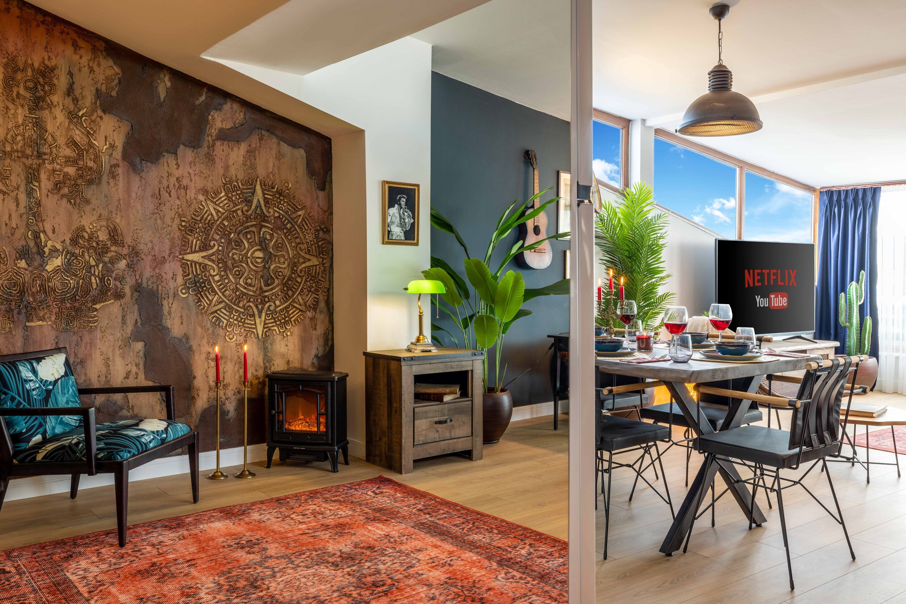 A modern living room with a fireplace, a dining area with a table set for six, and a large window with a view of the sky.