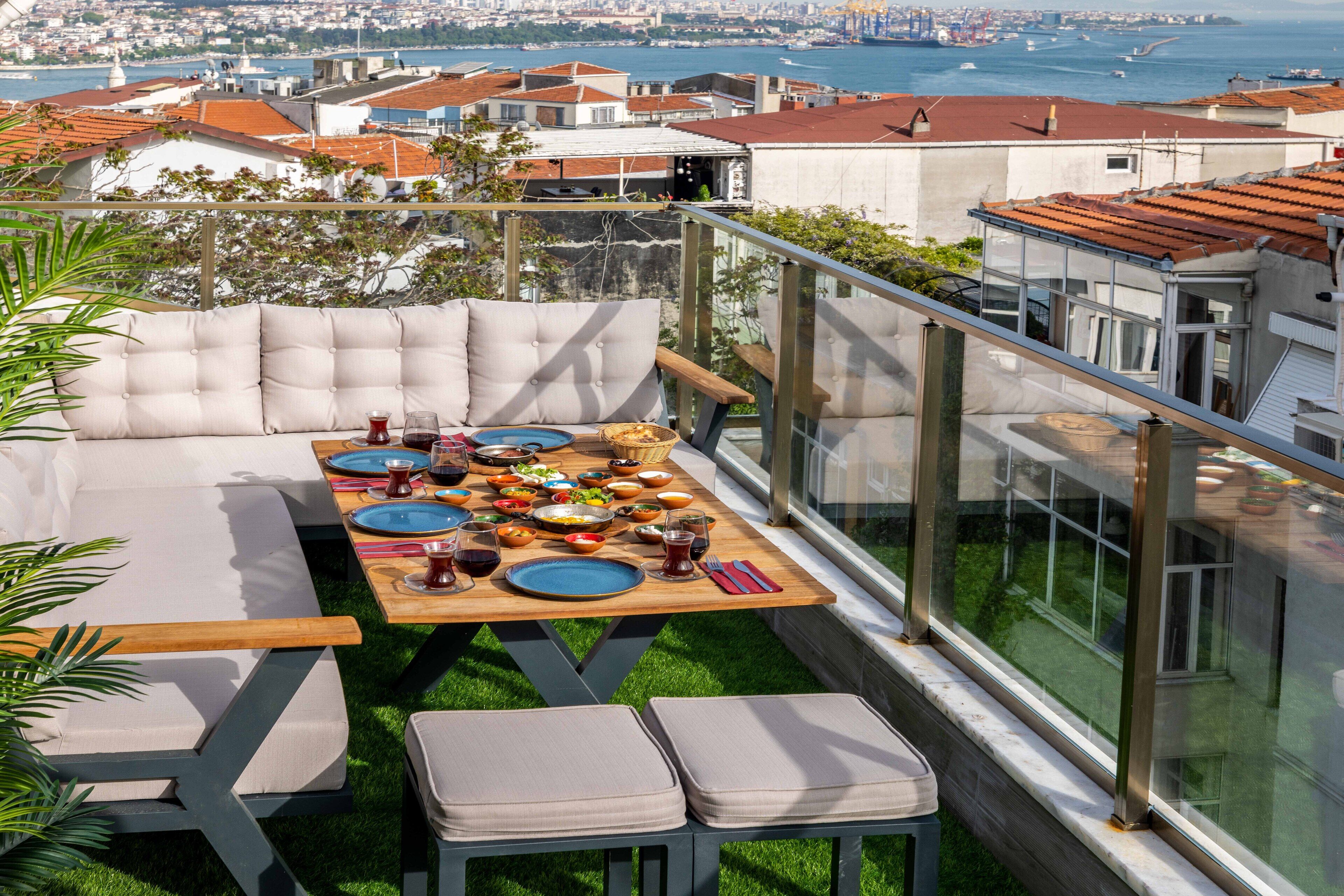 A rooftop terrace with a dining table set for a meal, surrounded by cushioned seating.