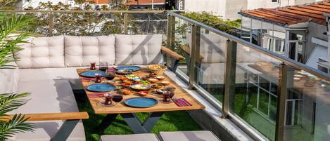 A rooftop terrace with a dining table set for a meal, surrounded by cushioned seating.