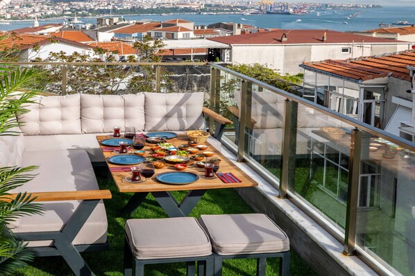 A rooftop terrace with a dining table set for a meal, surrounded by cushioned seating.