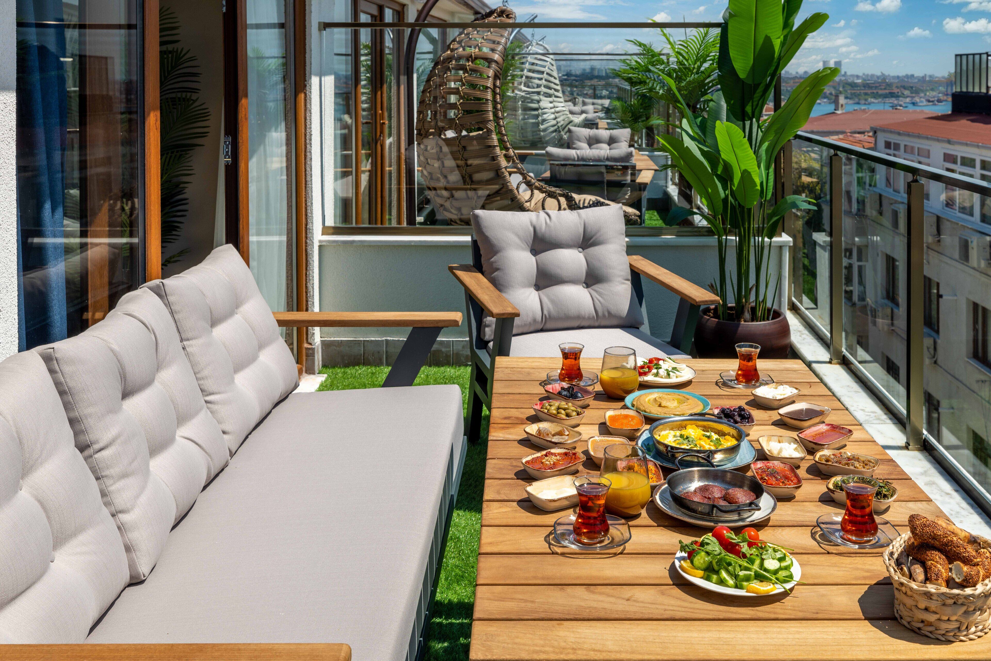 Un balcon avec une table en bois mise pour le petit-déjeuner, un canapé et un fauteuil suspendu.