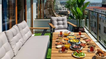 Un balcon avec une table en bois mise pour le petit-déjeuner, un canapé et un fauteuil suspendu.