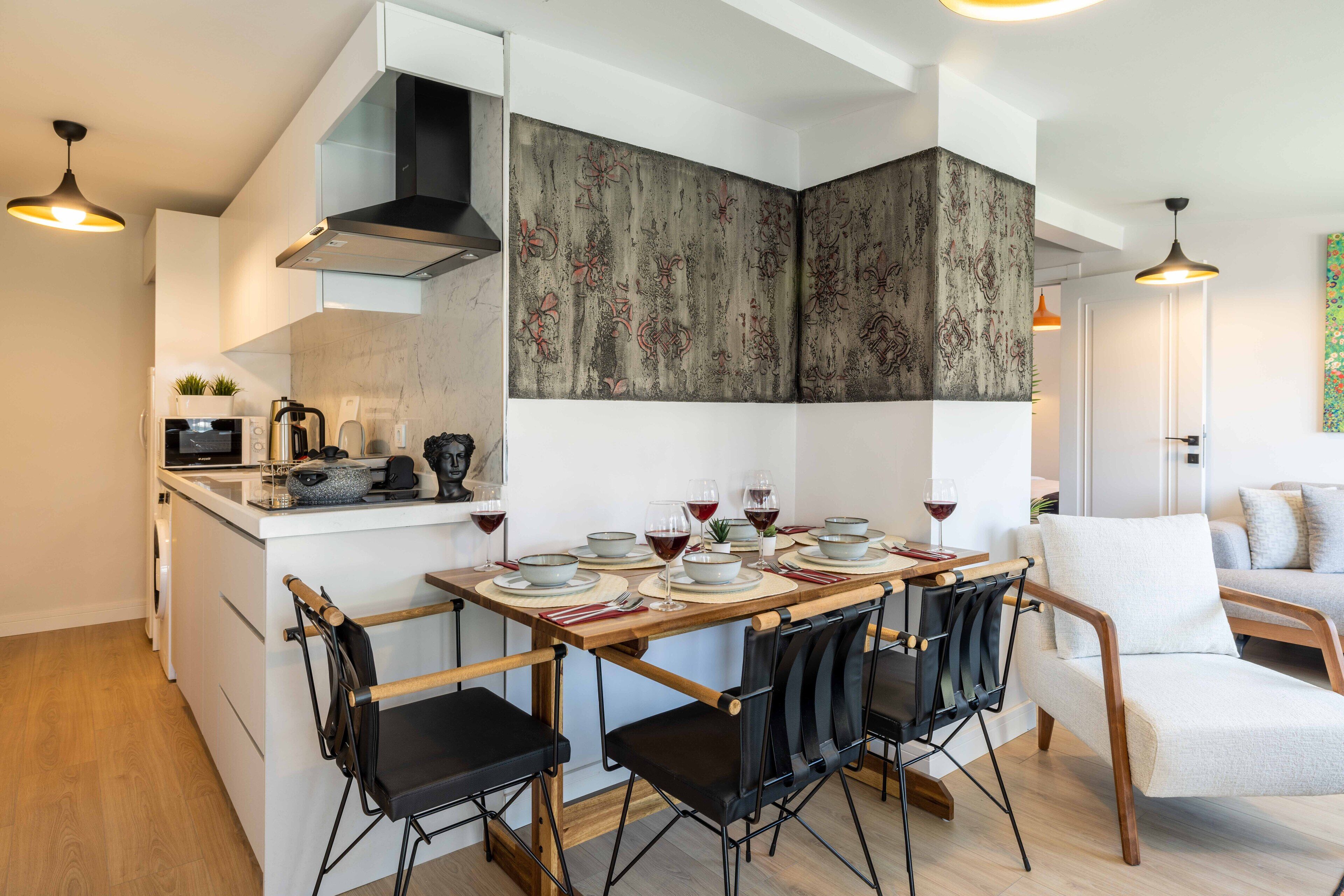 A modern kitchen with a central island, white cabinetry, and a dining area with four chairs and a table set for four.