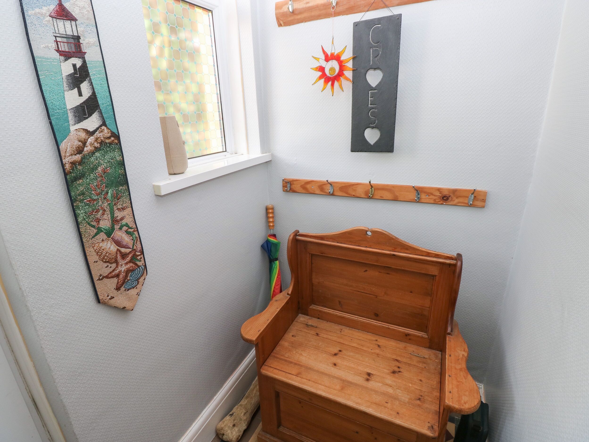 A wooden bench with a slatted seat and backrest, a wall-mounted coat rack, a decorative sun ornament, and a framed picture of a lighthouse.
