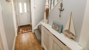 Een gang met een witte deur, een kamerbreed tapijt met dessin, een witte console met een model zeilboot en decoratie, en een trap met witte spijlen.