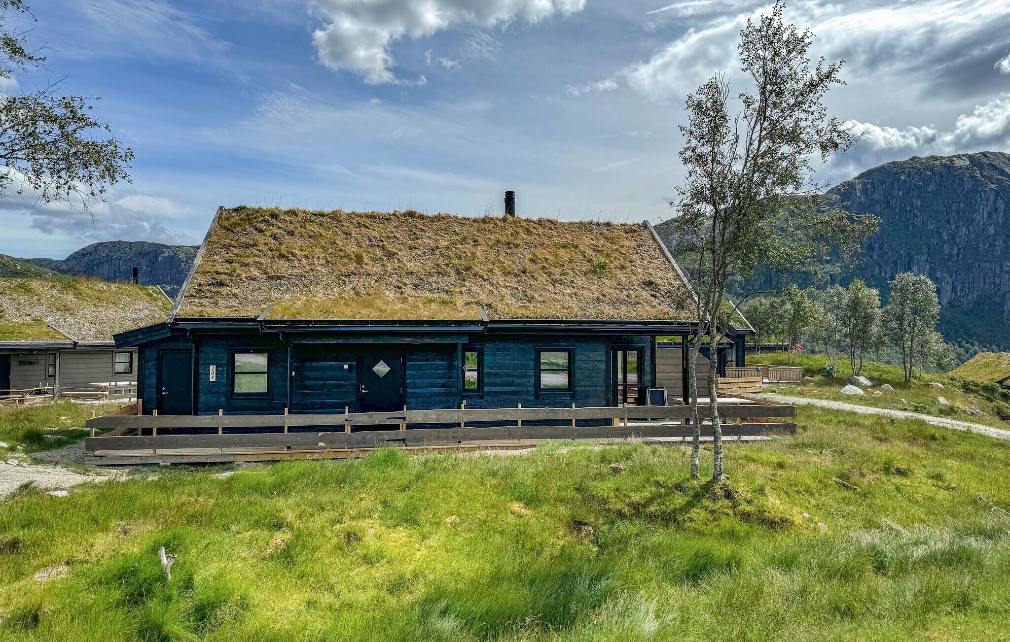 A rustic cabin with a thatched roof, situated in a grassy area with mountains in the background.