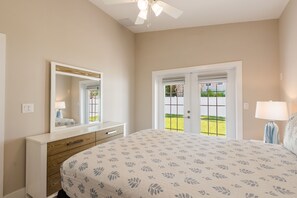 A bedroom with a large bed, a dresser, a mirror, and a door leading to a balcony.