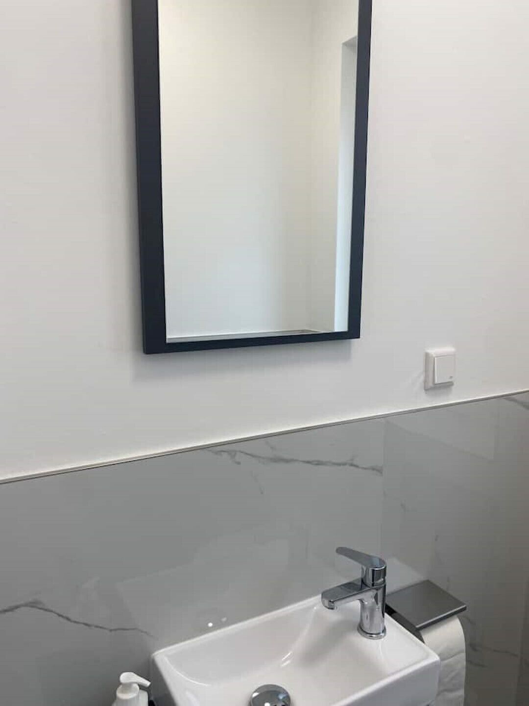 Une salle de bain avec un lavabo blanc, un miroir et un pare-baignoire en marbre.