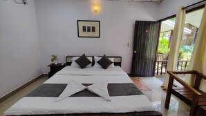 Una cama bien hecha con almohadas y una manta, una mesita de noche con una planta, un cuadro en la pared y vistas al exterior a través de una puerta.