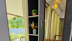 Una habitación con un espejo grande, un pequeño estante con plantas y vistas a un balcón con vegetación.